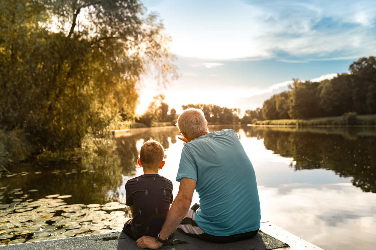 Grandfather and grandson sitting on a dock by a lake watching beautiful sunset, bonding, enjoying nature together